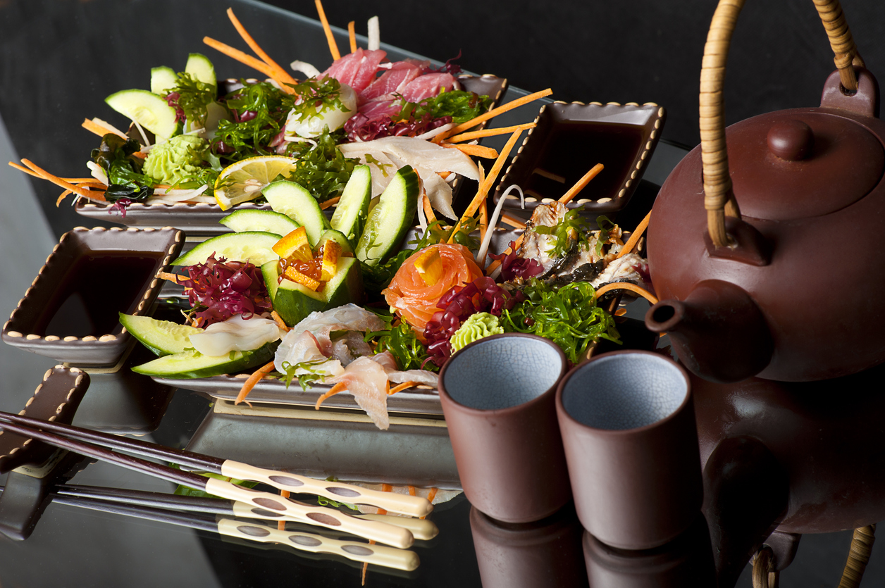 "Mixed sashimi, raw fish with cucumber on traditional japanese plate. soy sauce and clay teapot and cups"