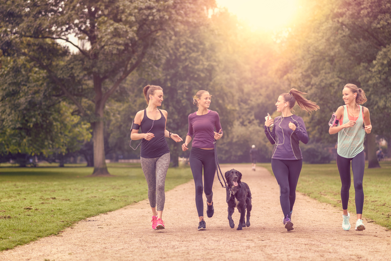 Four Healthy Young Women Jogging at the Park in the Afternoon with a Pet Dog.
