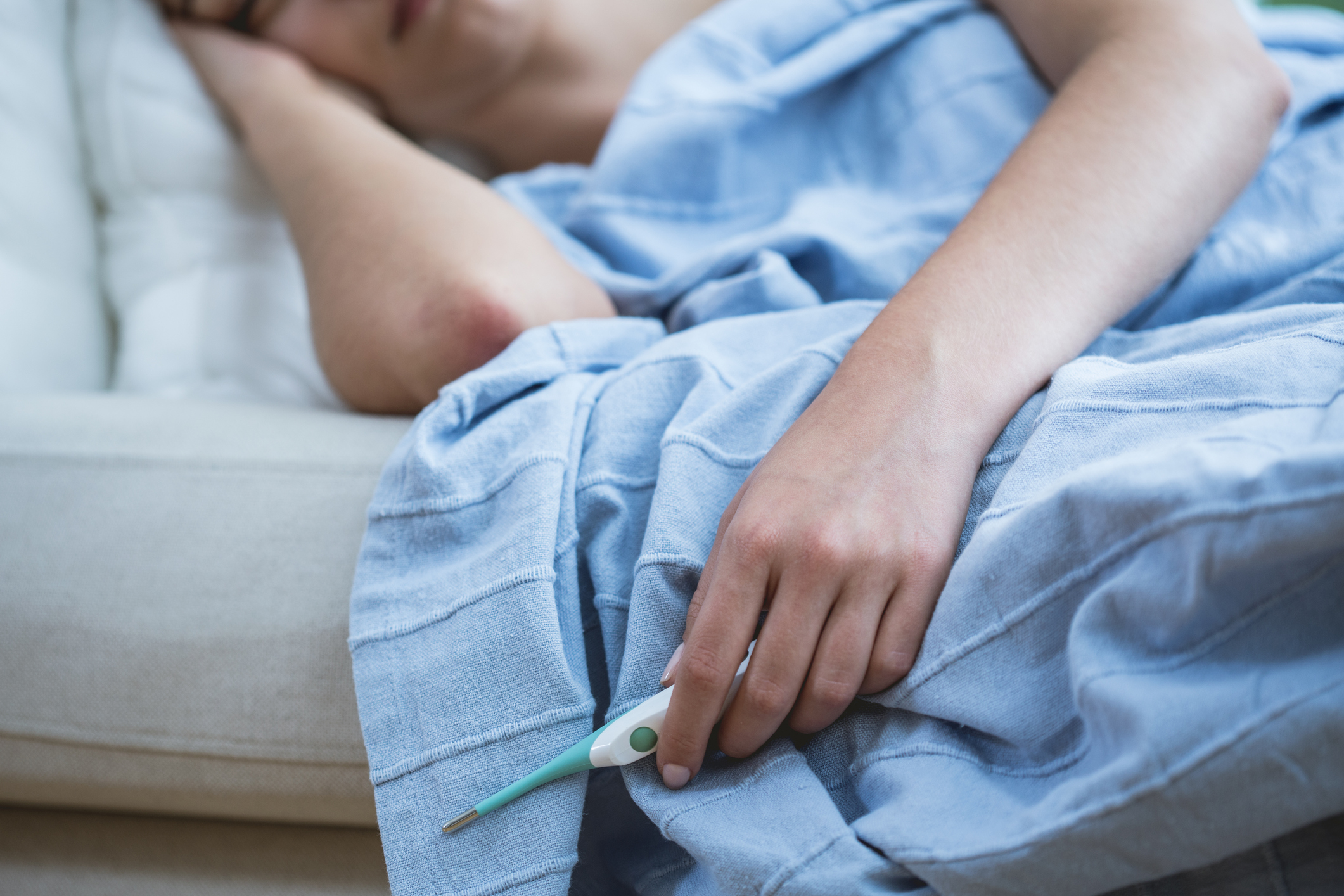 Close-up of ill woman in bed holding thermometer