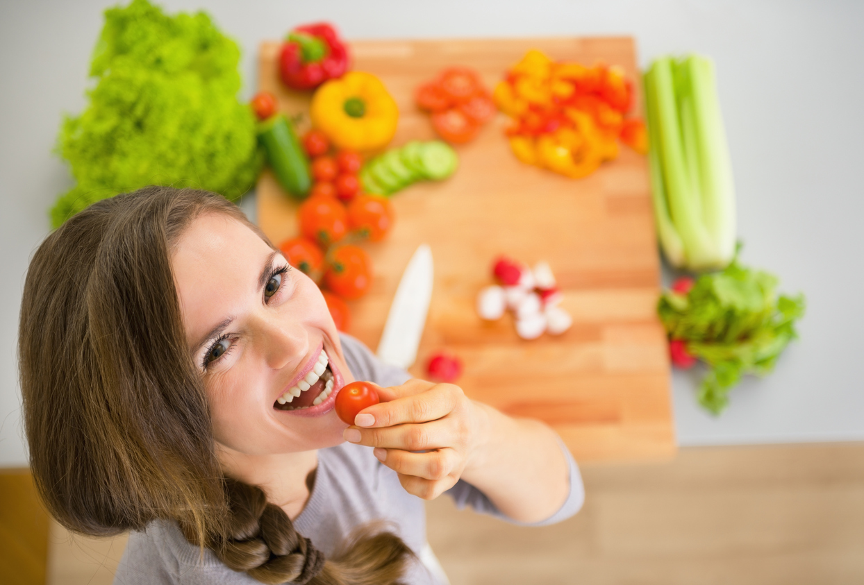 Portrait of happy young housewife with vegetables in kitchen