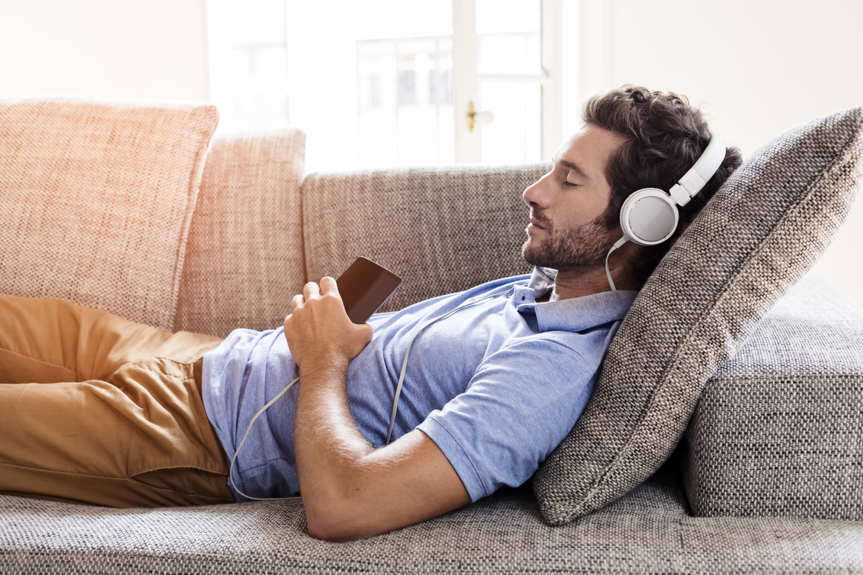 Young male couch listen headphones mobile phone at home