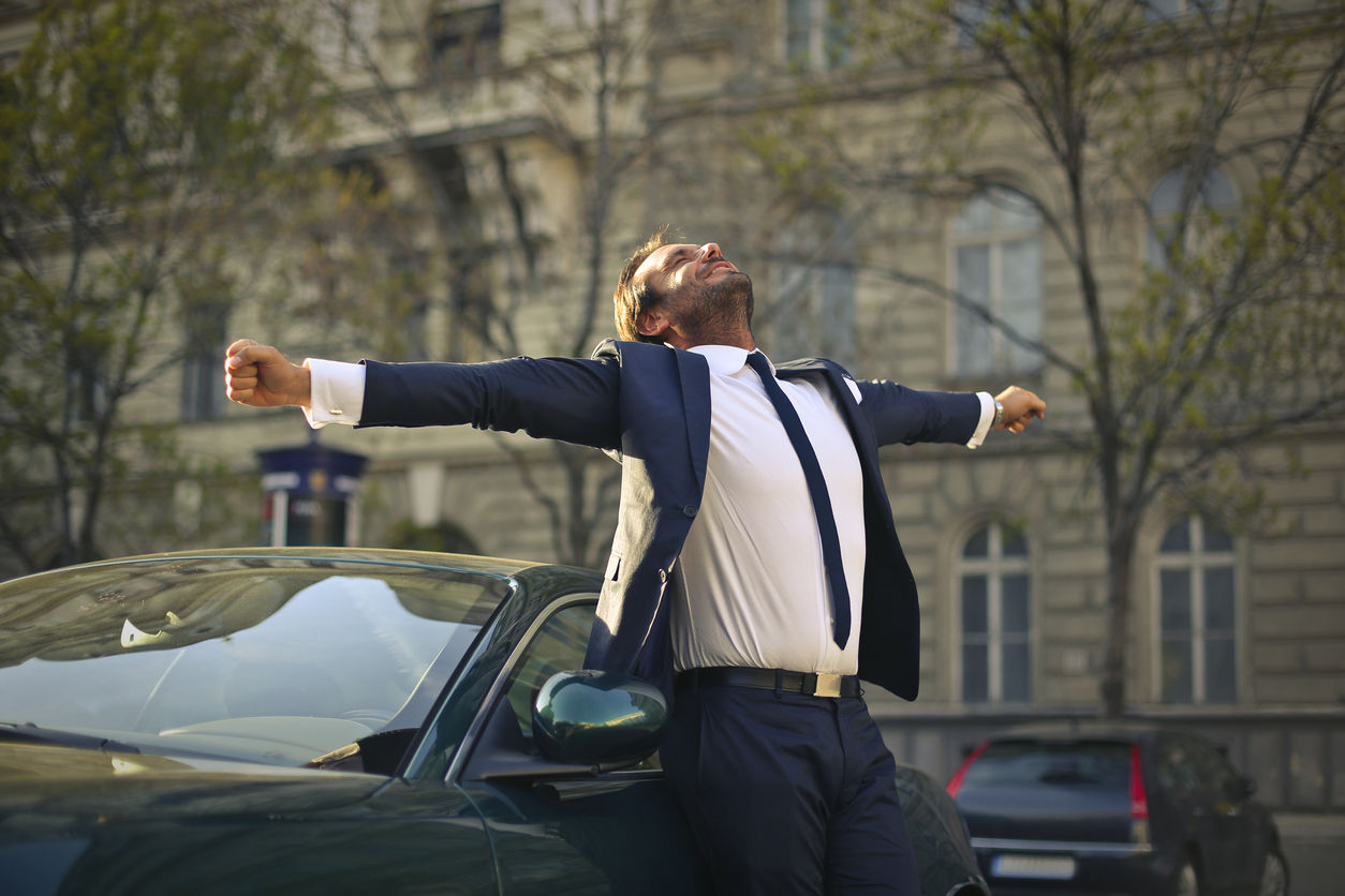 Elegant businessman on the street next to his car tilting his head back being extremely happy