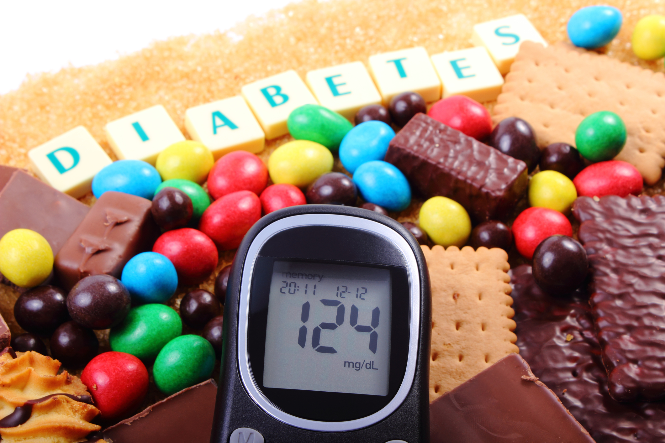 Glucose meter with word diabetes, heap of candies, cookies and brown cane sugar, too many sweets, unhealthy food, concept of diabetes and reduction of eating sweets