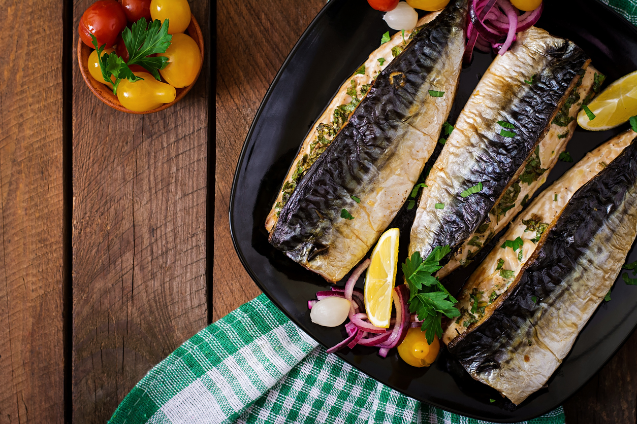 Baked mackerel with herbs and garnished with lemon and pickled vegetables. Top view