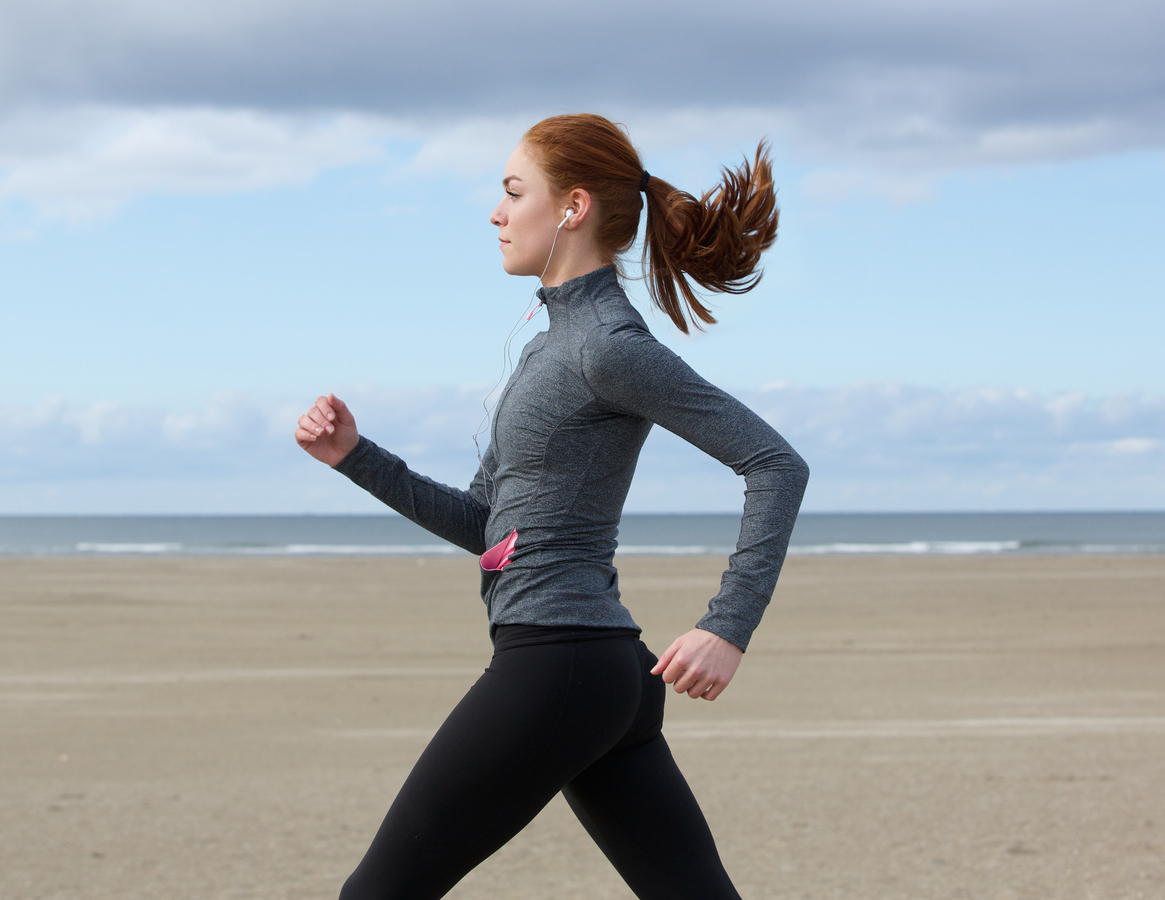 Side view portrait of a young woman running by the beach