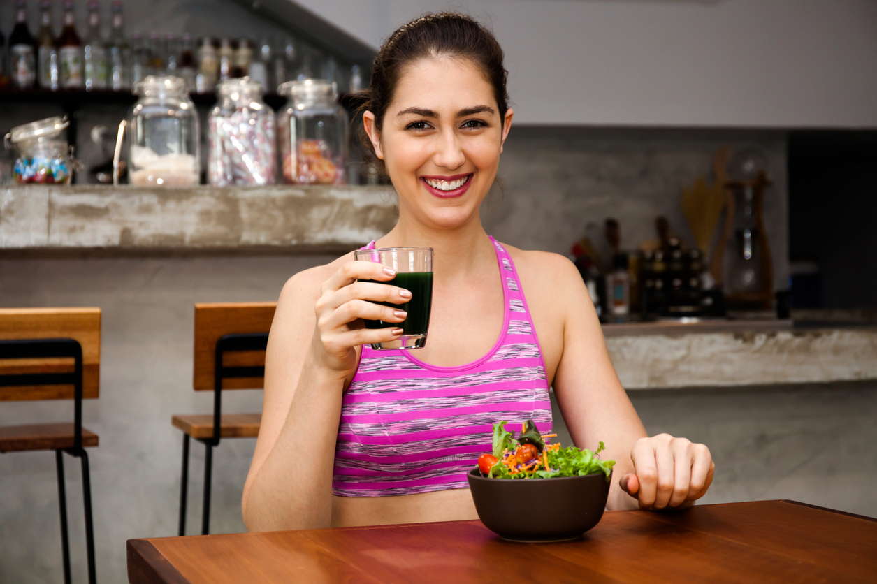 Attractive fitness woman is eating salad with healthy juice