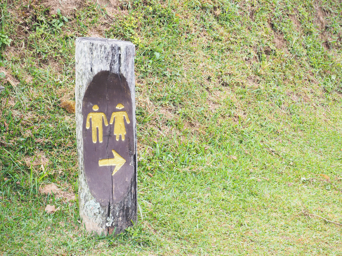 Outdoor public restroom sign on wood over grass field in the national park.