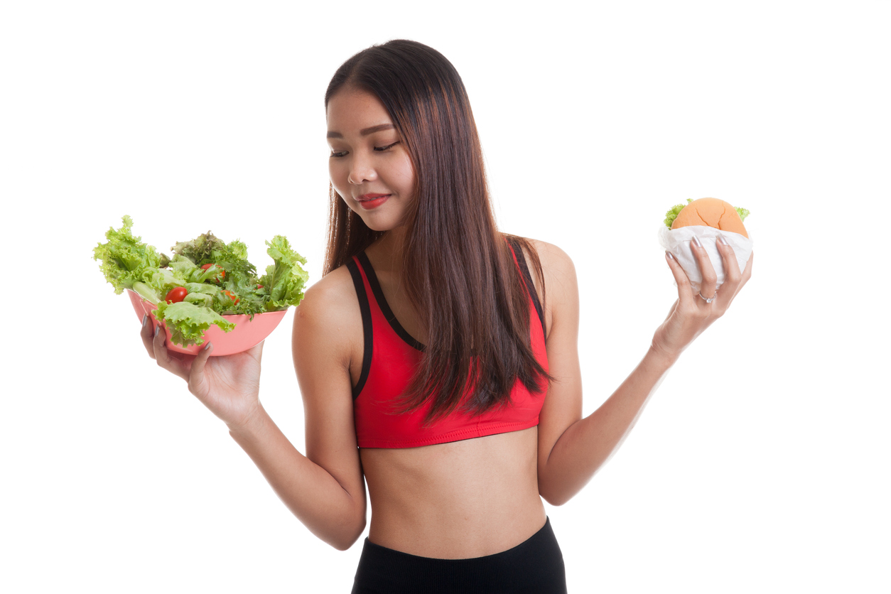 Beautiful Asian healthy girl with salad and hamburger isolated on white background.