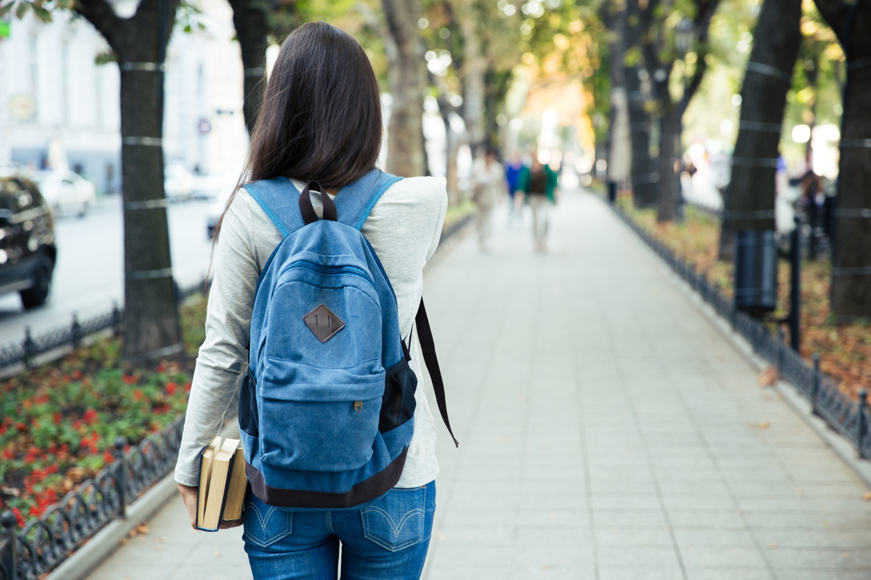 Back view portrait of a female student walking in the city park outdoors