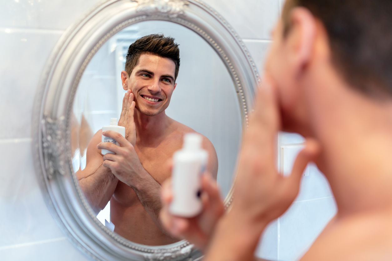 Healthy positive male treating sking with lotion after shaving