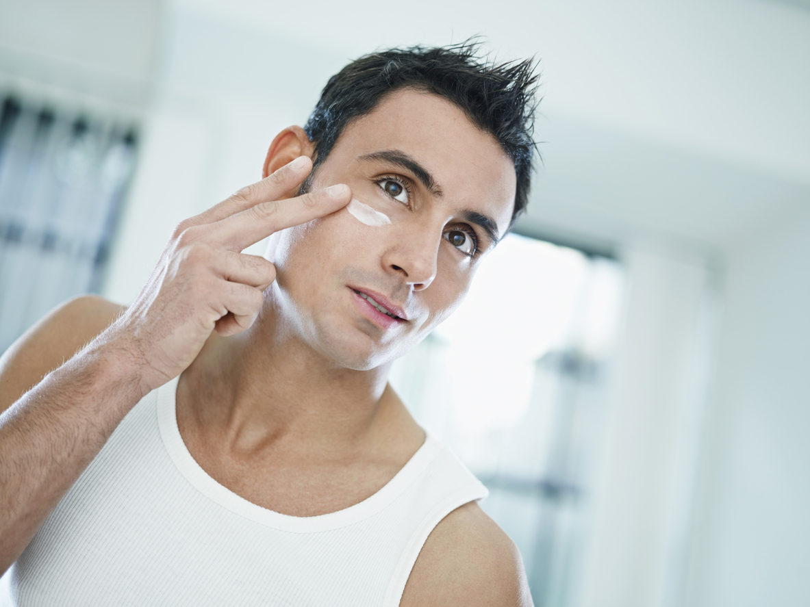 young caucasian man applying eye cream on face. Horizontal shape, front view, head and shoulders