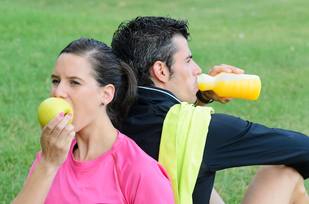Couple of athletes taking a break, eating an apple and drinking isotonic drink.