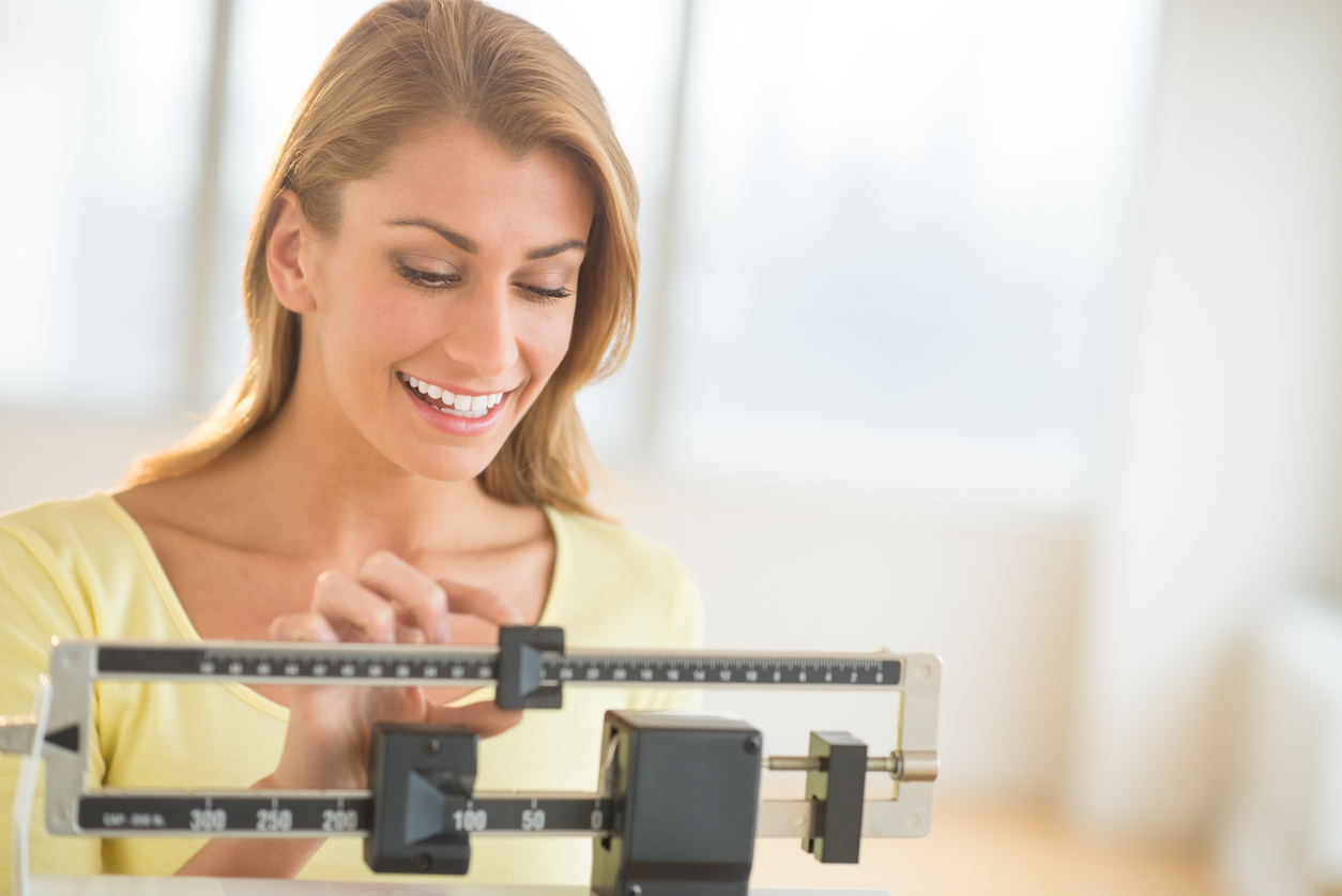 Happy young woman weighing herself on balance scale at health club