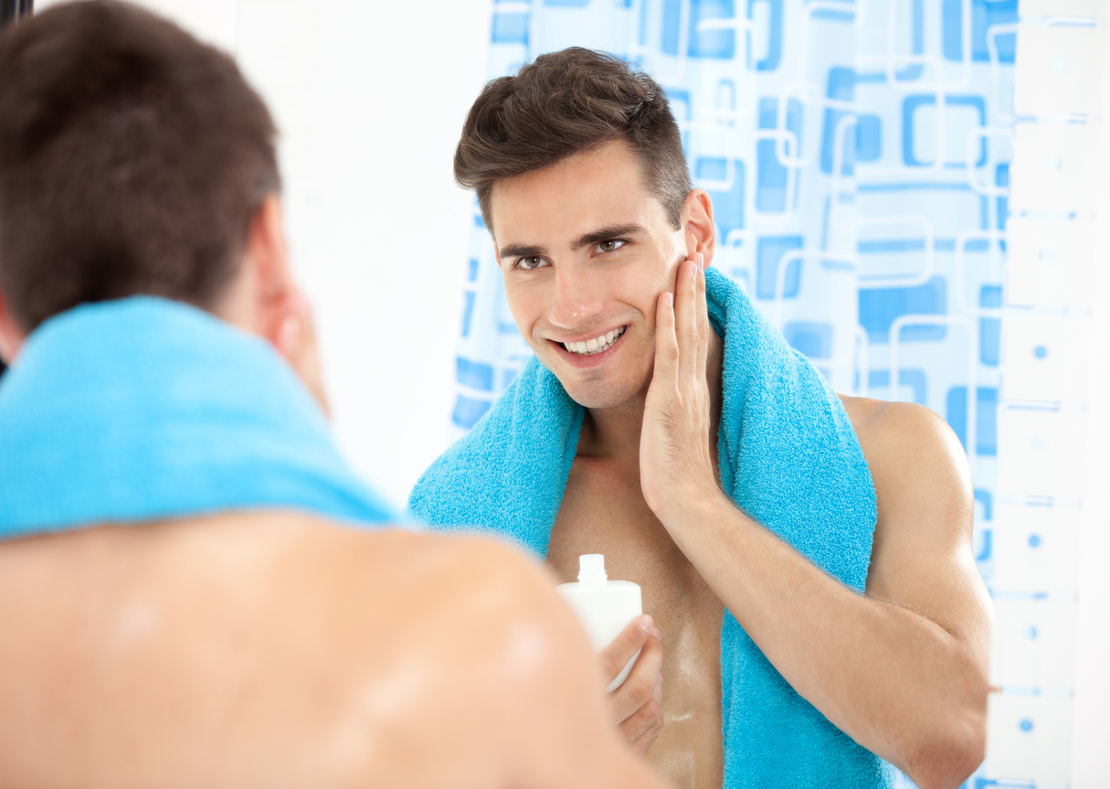Portrait of a young man in the bathroom applying after shave