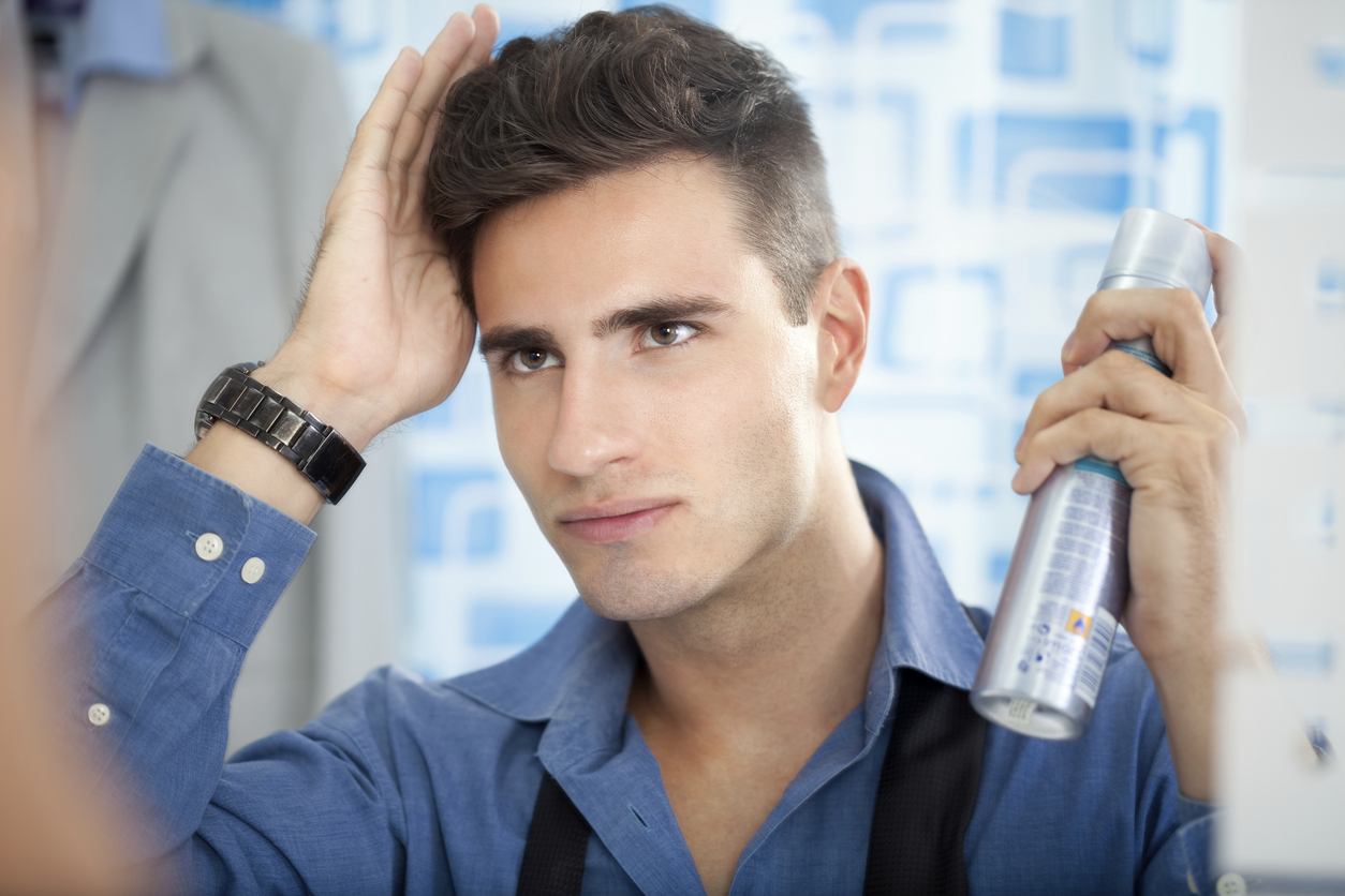 Young man applying hair spray to his hair.