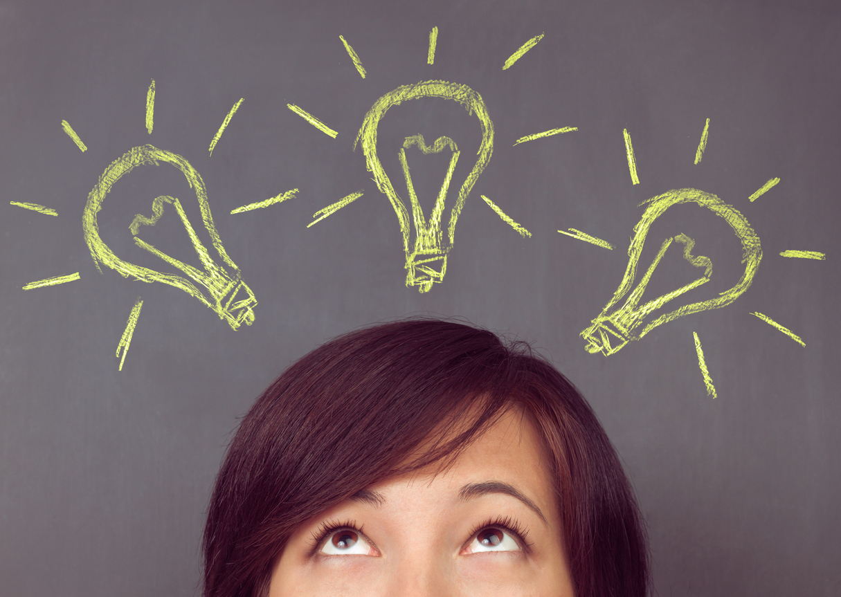 Young woman looks up on light bulb on the background of blackboard, concept of new ideas