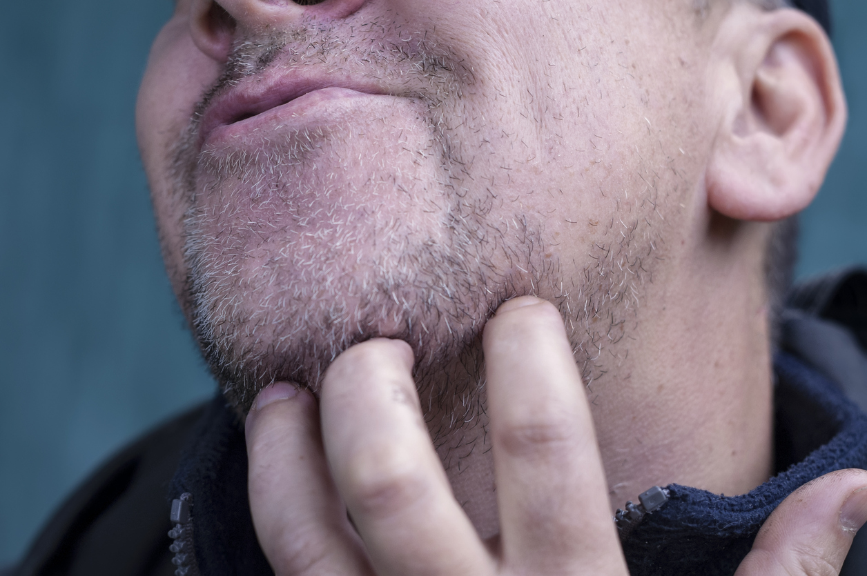 Matured sneering man scratching his unshaven chin, outdoor cropped shot