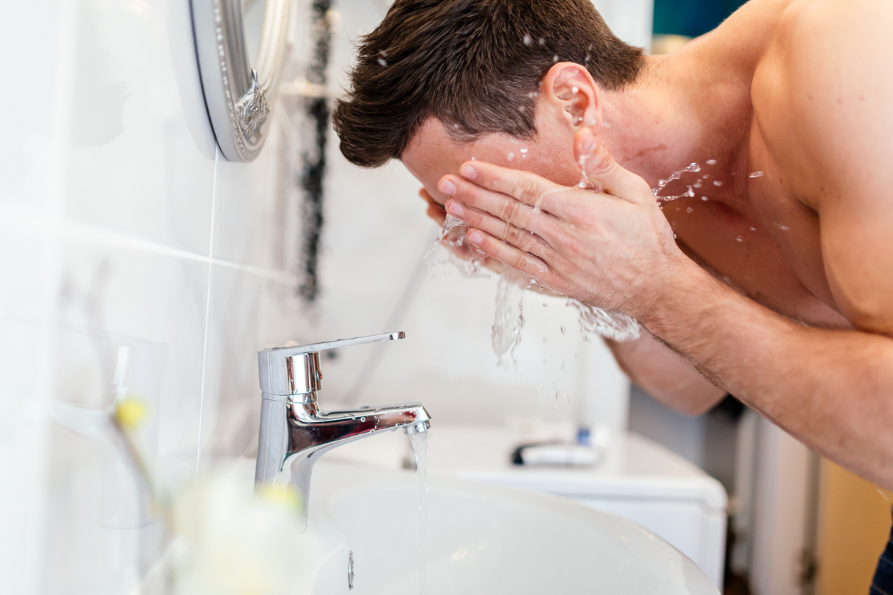Handsome man washing face in bathroom in morning