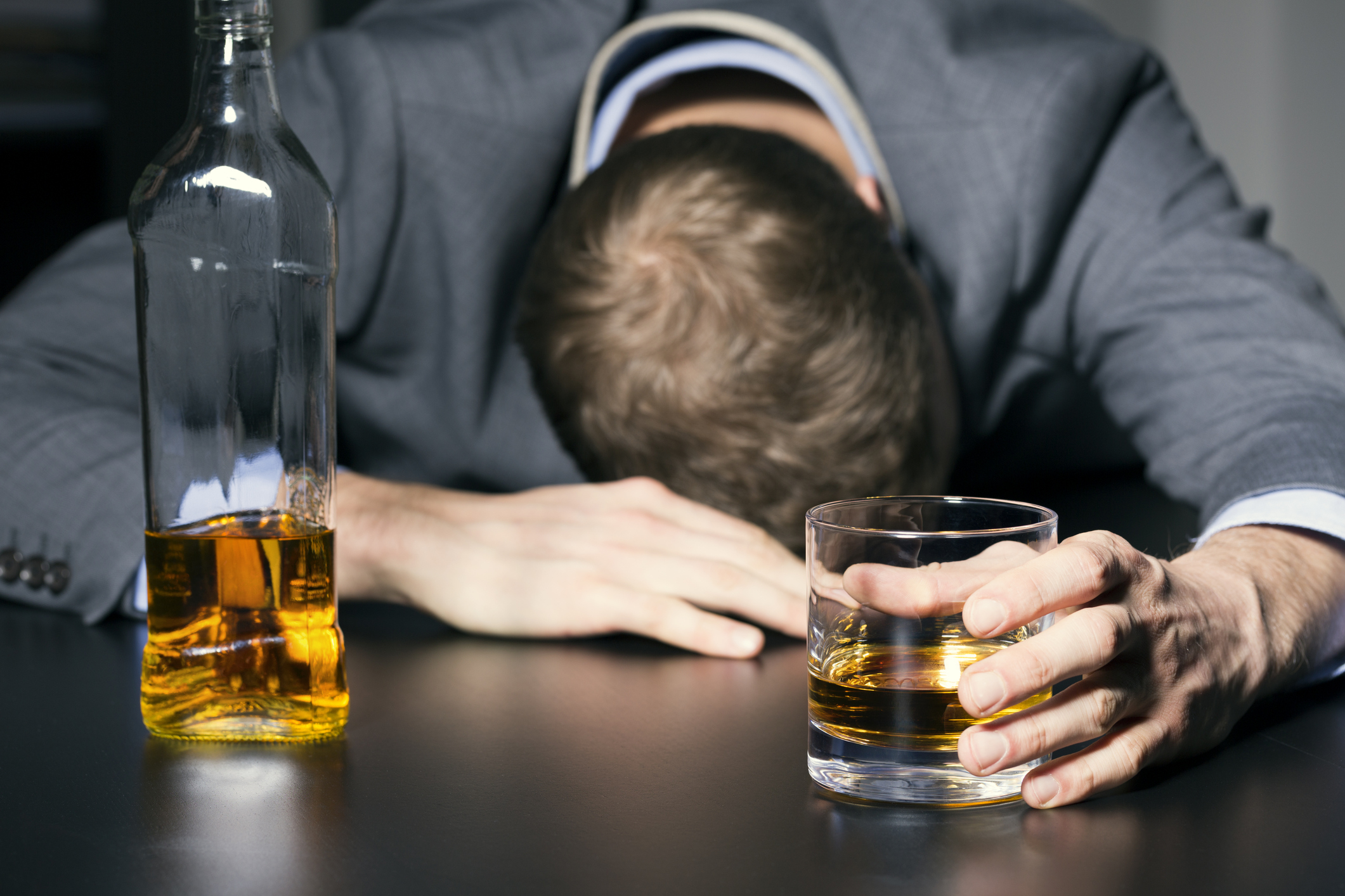 alcohol addiction - drunk businessman holding a glass of whiskey on the table