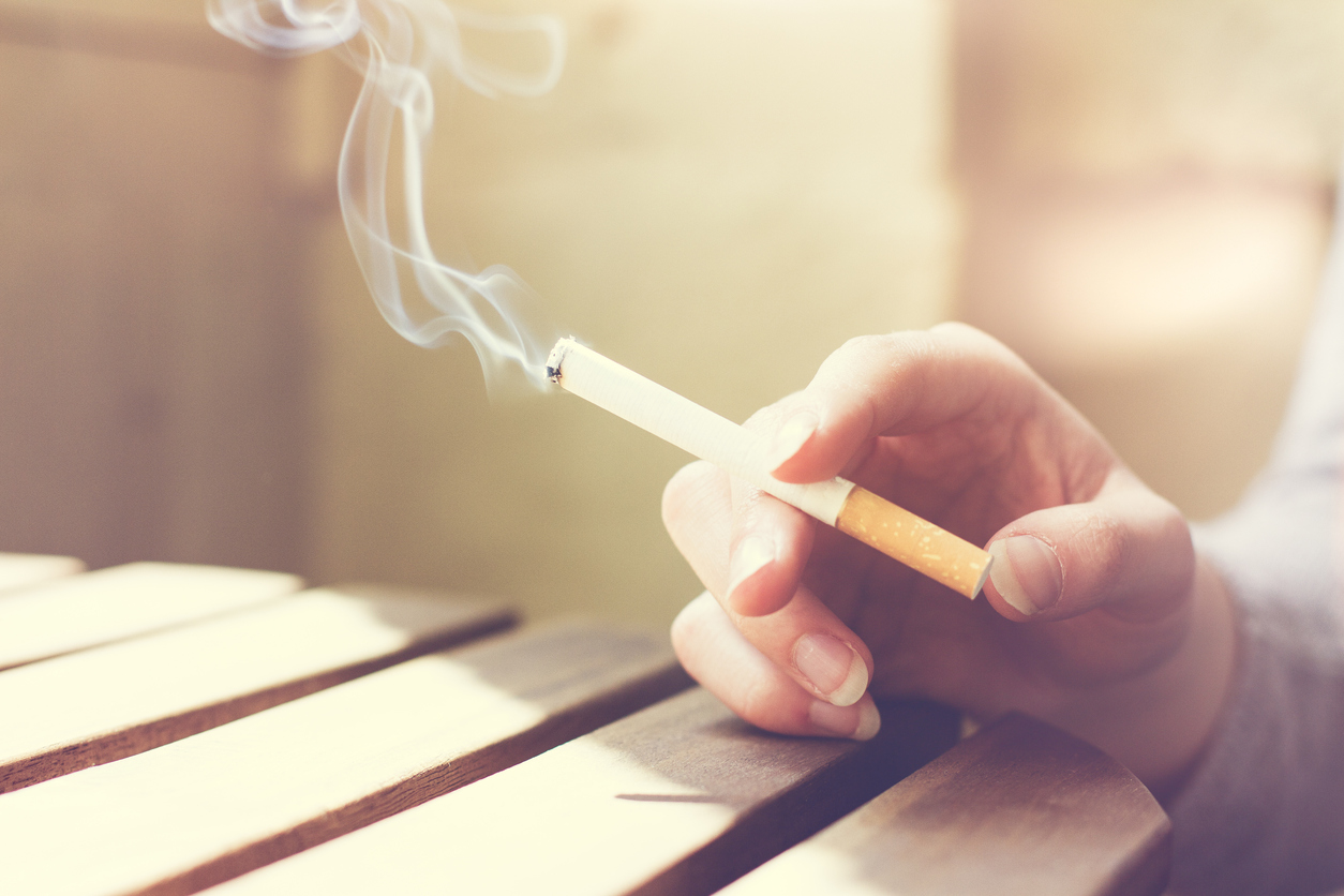 Woman smoker smoking a filter tip cigarette with her hand resting on a slatted wooden table with copy space, close up view