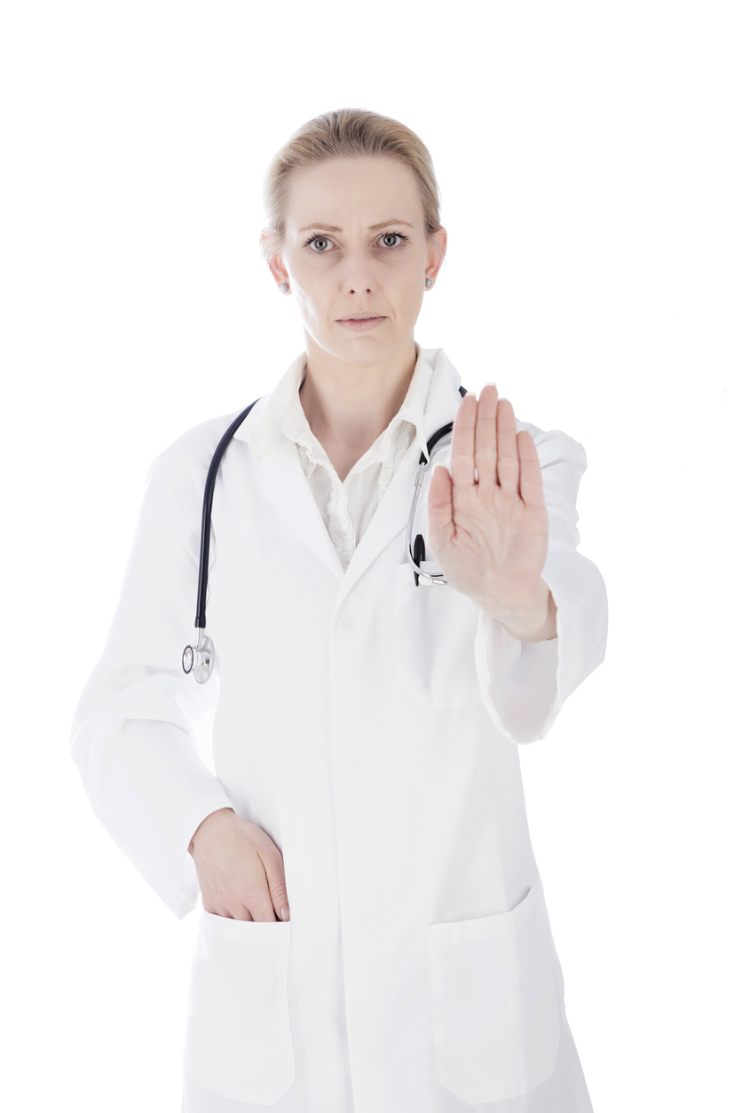 Close up Portrait of a Serious Female Doctor Showing Stop Hand Sign with One Hand in her Pocket and Looking at the Camera. Isolated on White Background.