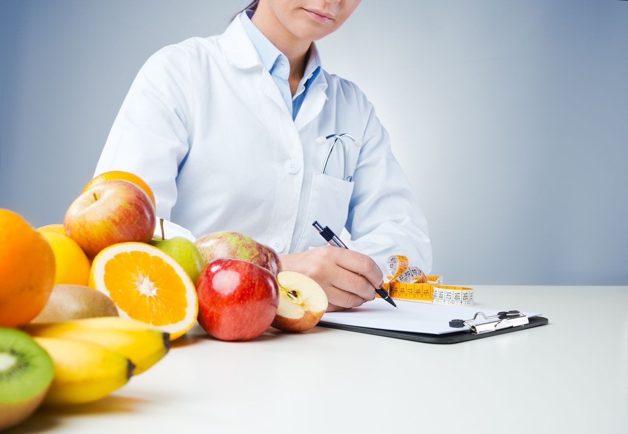Professional nutritionist working at desk and writing medical records with fresh fruit on foreground