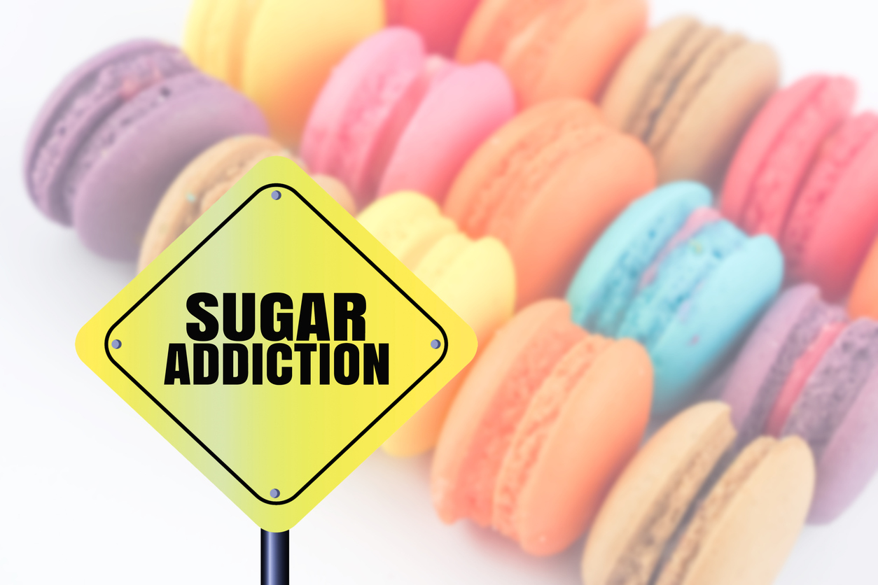 word sugar addiction on yellow caution sign blurred colorful sweet macaron