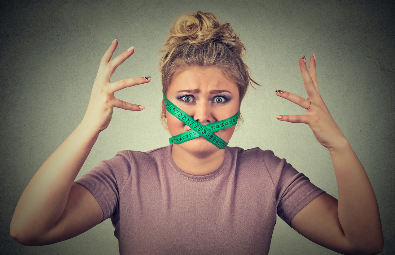 New diet restriction and stress concept. Portrait of young frustrated woman with a green measuring tape around her mouth isolated gray background. Human face expression emotion. Healthy lifestyle