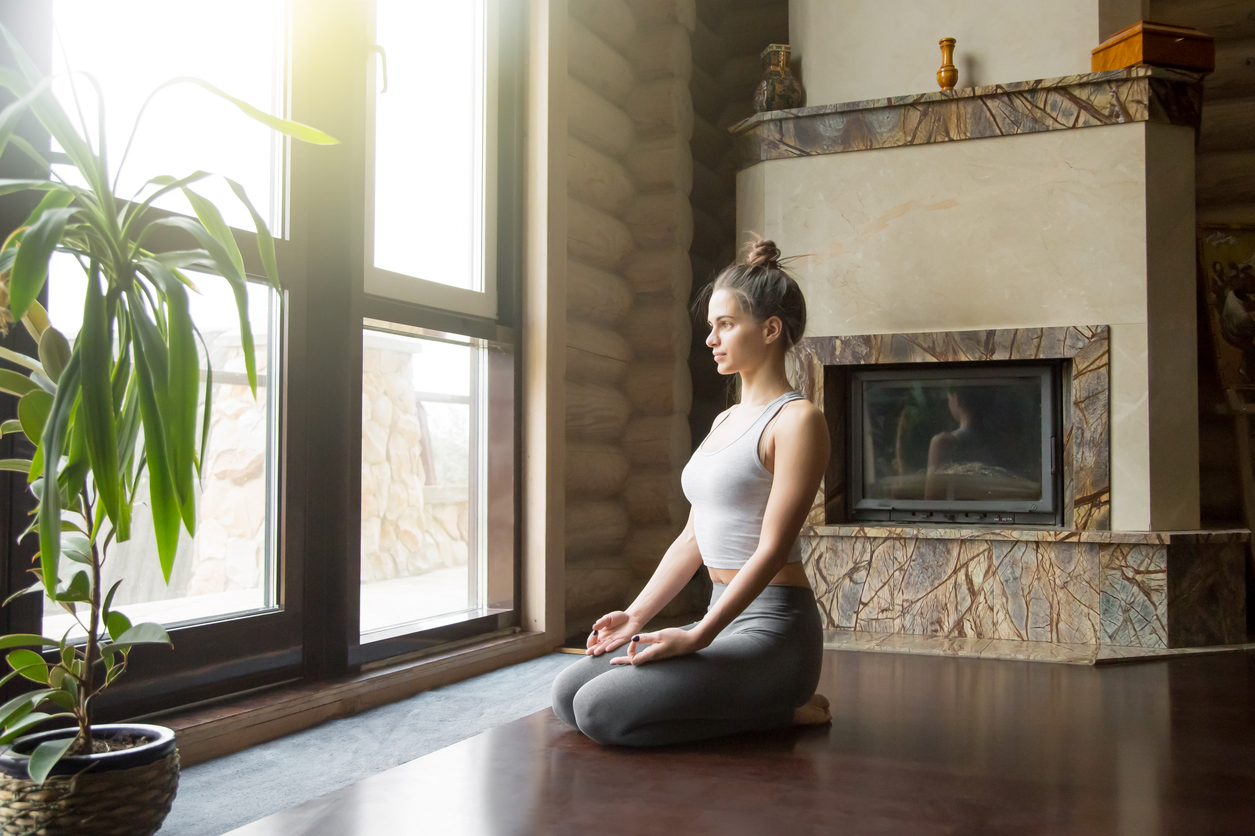 Young attractive woman in vajrasana pose, home interior backgrou