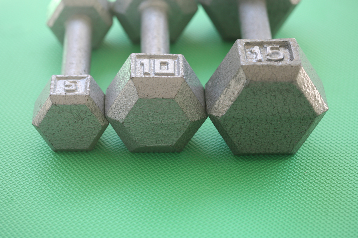 Horizontal orientation photograph of 5, 10 and 15 pound weights in a row on a green mat