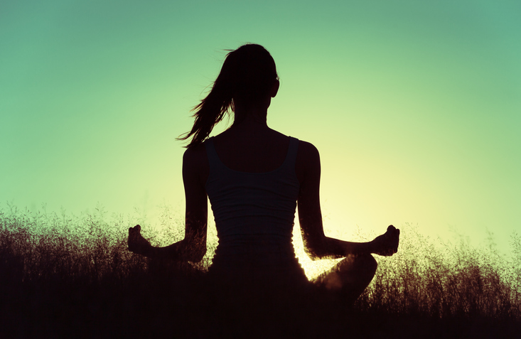 Woman meditating in the field during sunset.